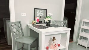 A white dining table with a shelf, two grey chairs, and a decorative item resembling a ballerina.