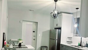 A modern kitchen with a stainless steel refrigerator, a dining area with a white table and grey chairs, and a hanging light fixture.