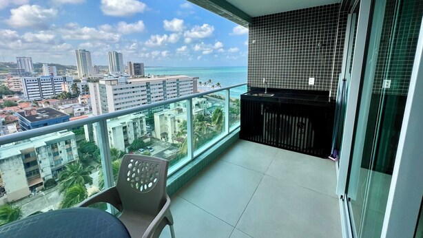 A balcony with a view of the ocean and cityscape, a small seating area, and a tiled backsplash. - RN STUDIO - APTO 903 (Maceio)