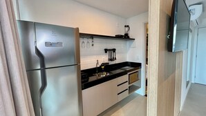 A modern kitchen with a stainless steel refrigerator, black countertop, white cabinets, and a built-in oven. - RN STUDIO - APTO 903 (Maceio)