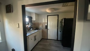 Una cocina estrecha con armarios blancos, un refrigerador negro y una puerta que da a otra habitación.