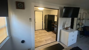 Una habitación con piso de madera, un tocador blanco, un televisor de pantalla plana y una estantería.