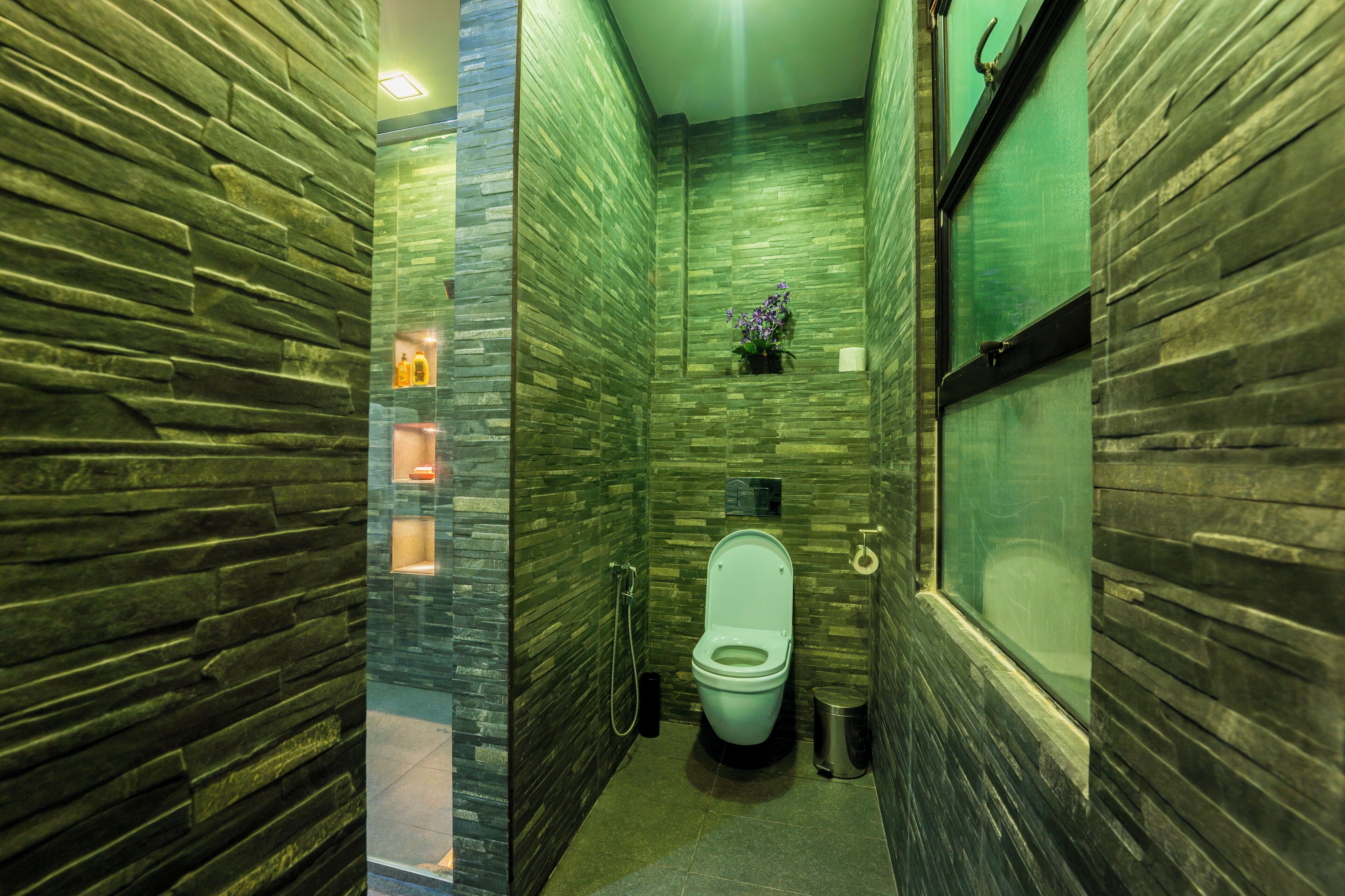 A bathroom with a stone wall design, a toilet, a hand dryer, and a trash bin.