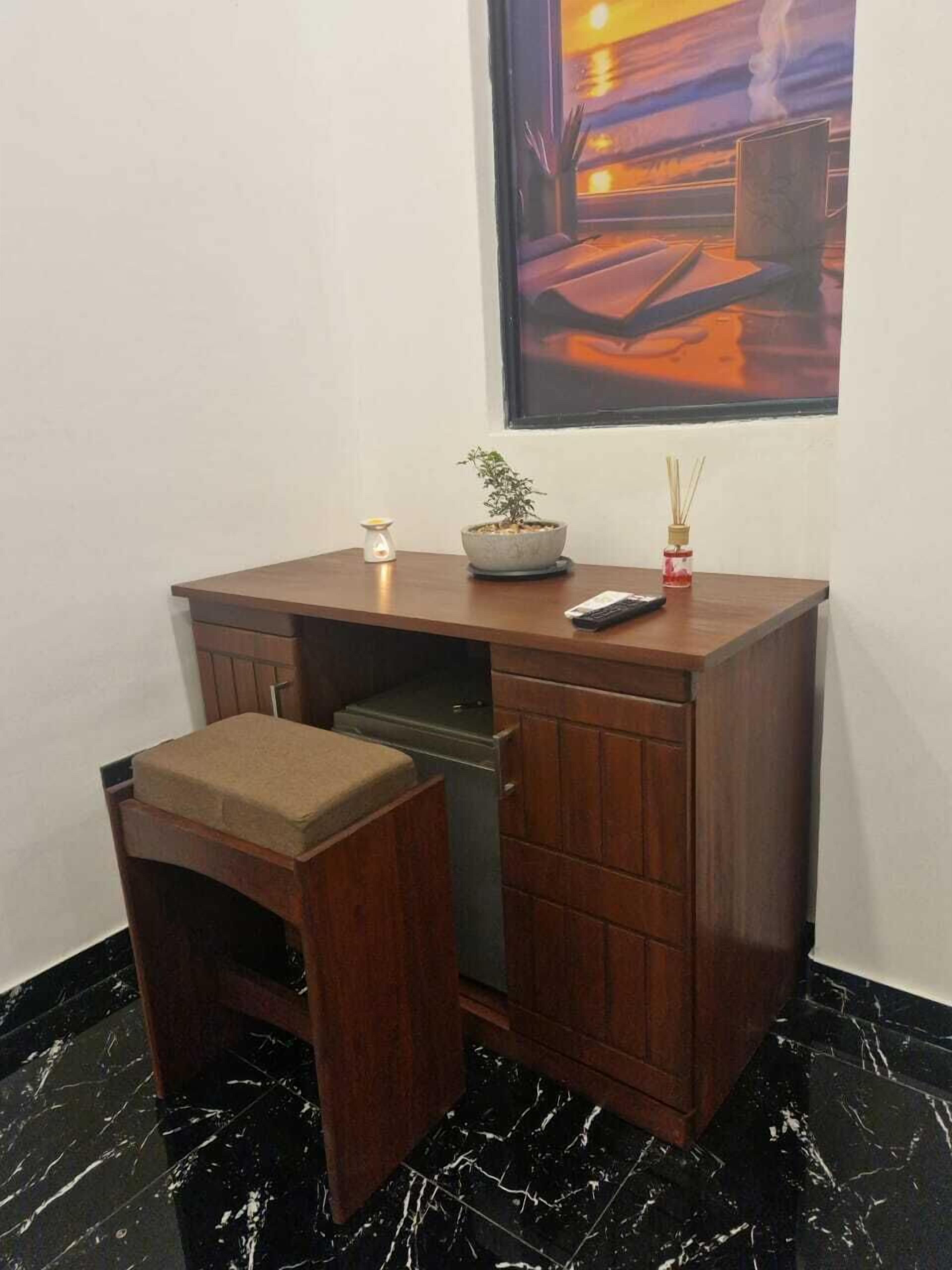 A small wooden desk with a bench, a potted plant, a candle, and a mobile phone.