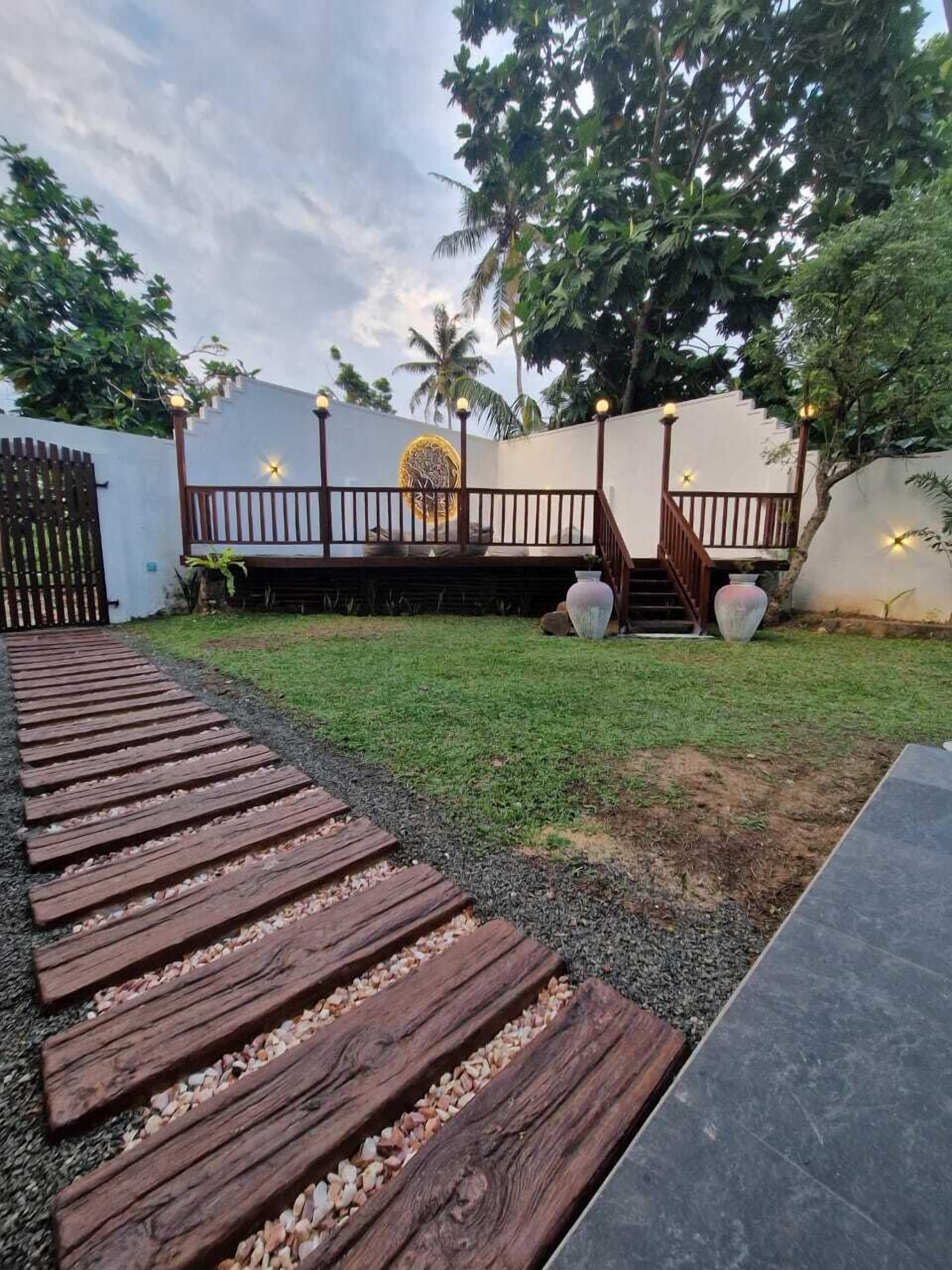 A wooden deck leading to a white wall with a decorative emblem, a staircase, and a paved area with pebbles.