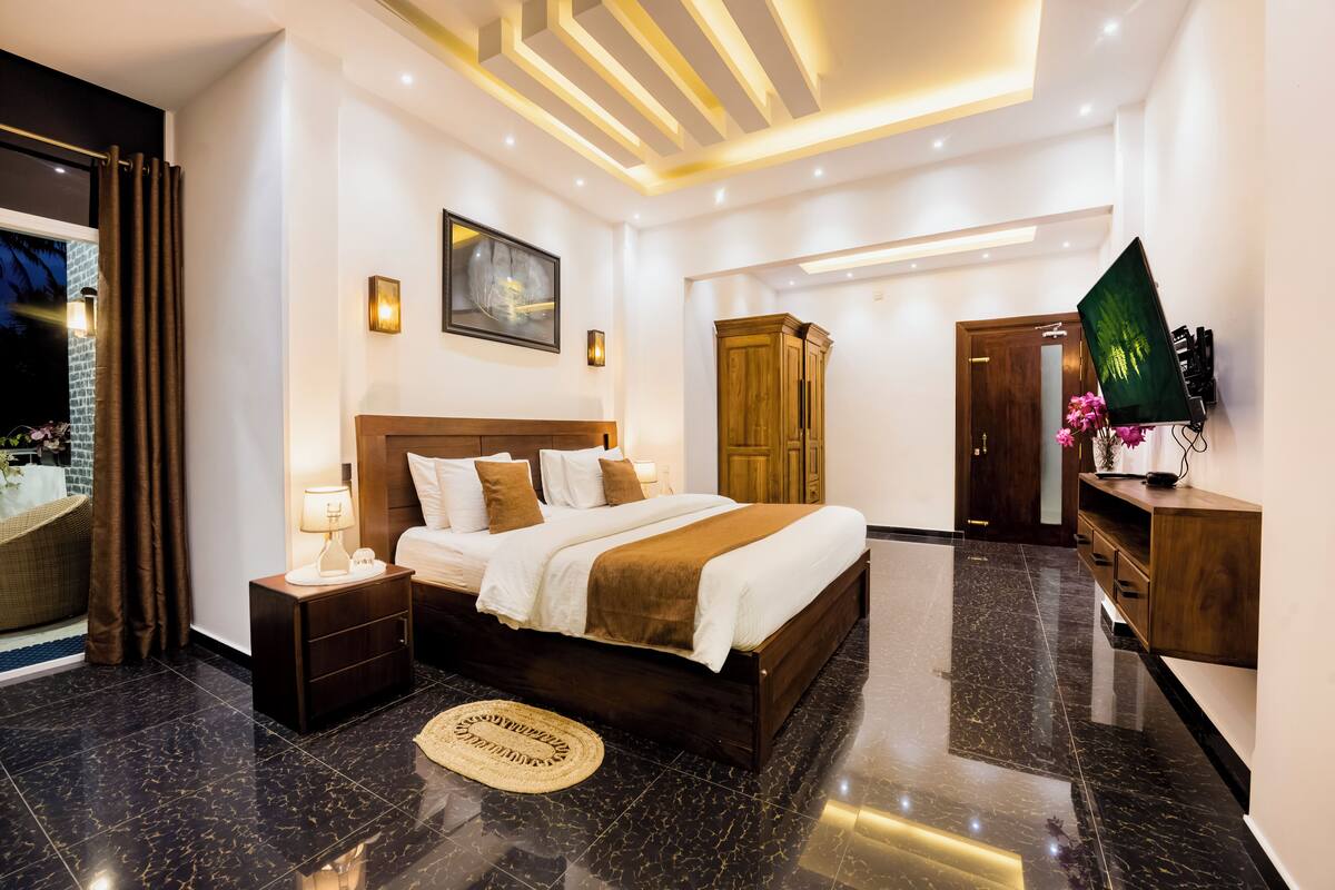 A modern bedroom with a large bed, a wooden wardrobe, a flat-screen TV, and a decorative wall piece.