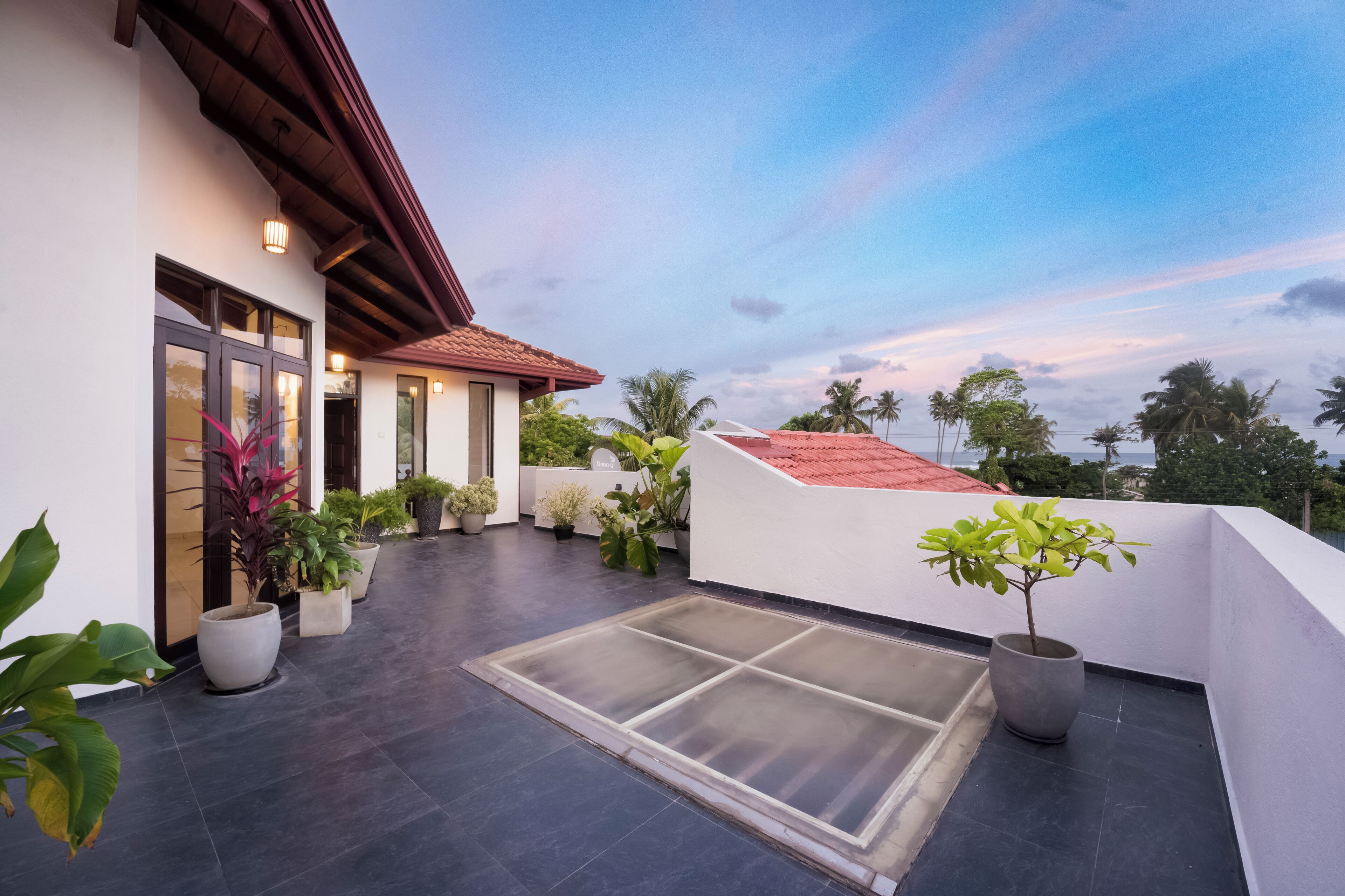A rooftop terrace with potted plants, a glass door entrance, and a view of the sky.