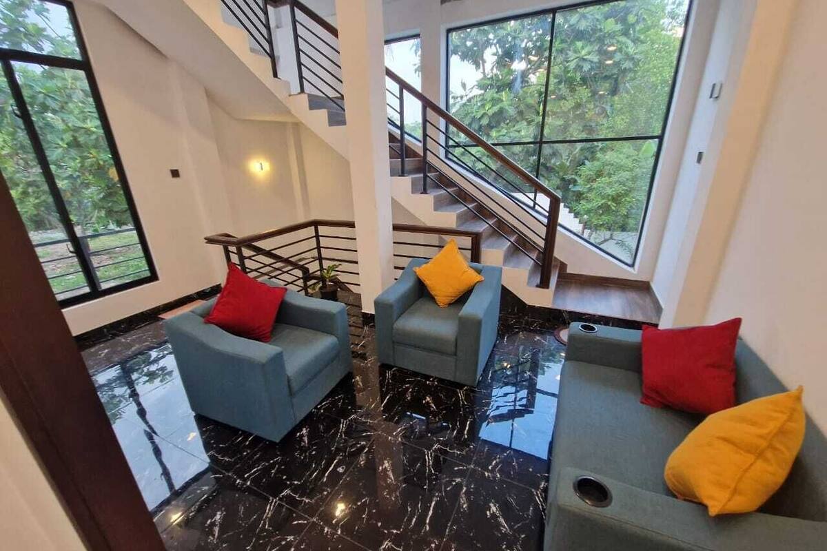 A spacious living area with a black marble floor, two blue sofas with red and yellow cushions, and a staircase leading to an upper level.