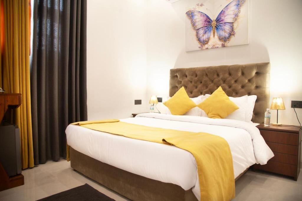 Una habitación de hotel con una cama grande, un cabecero capitonado y una obra de arte con temática de mariposas en la pared.