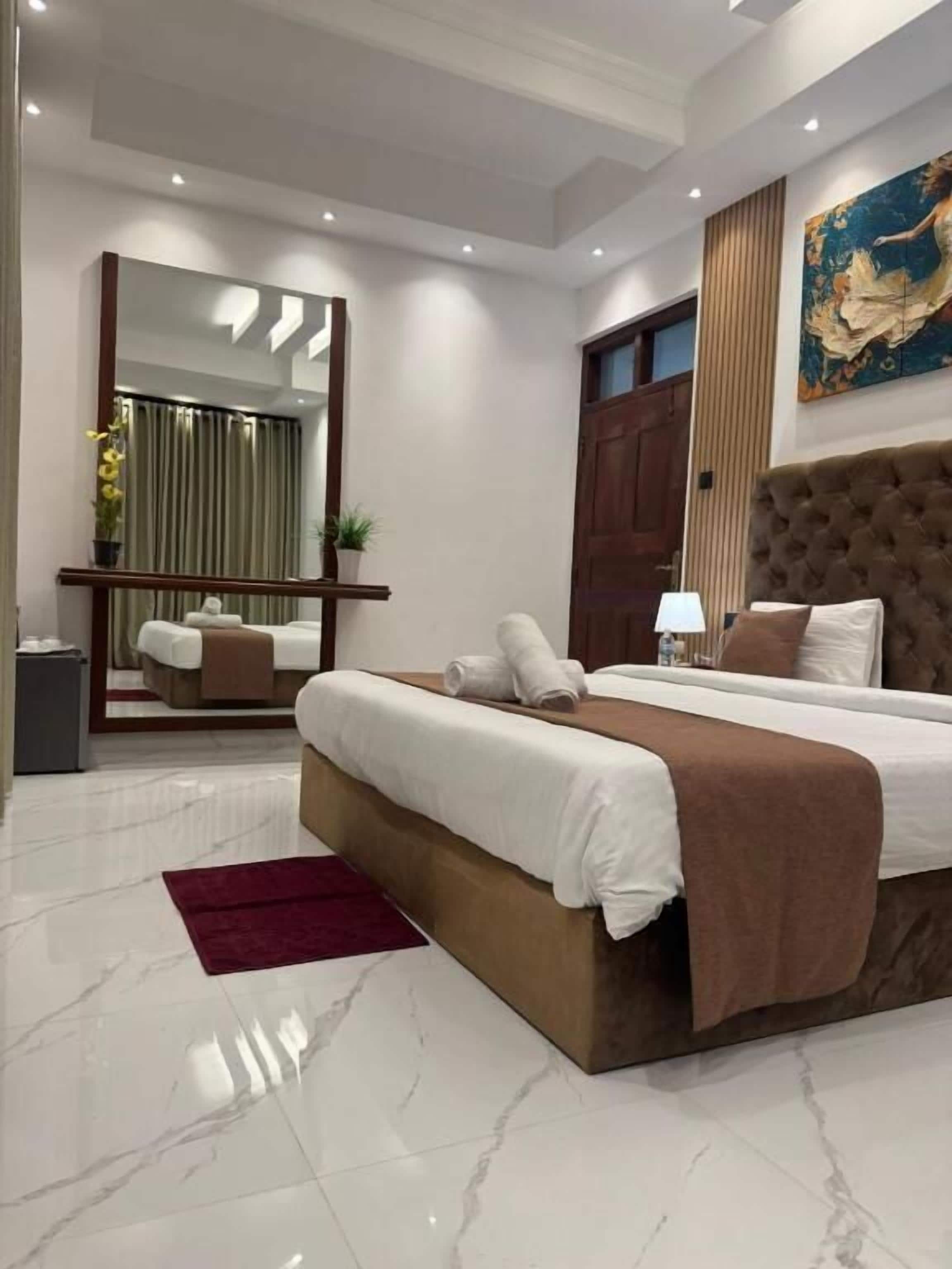 Une chambre d’hôtel moderne avec un grand lit, un miroir, une tête de lit en bois et un tableau au mur.