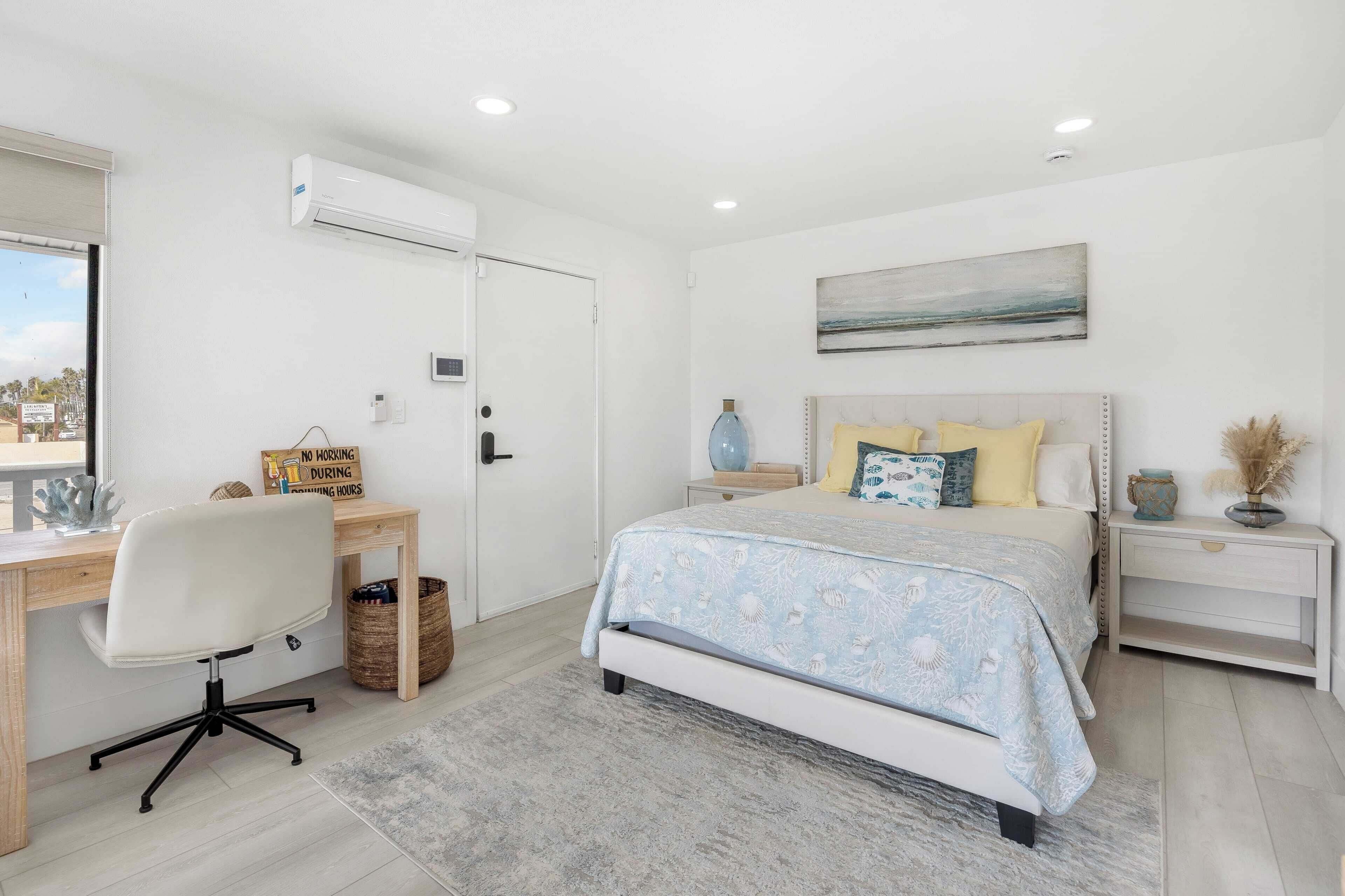 A bedroom with a bed, bedside tables, a desk, and an air conditioning unit.