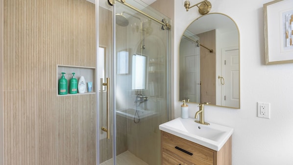 Et moderne badeværelse med en glasafskærmet bruseniche, et stort spejl og et toiletbord med vask.