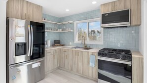 A modern kitchen with a stainless steel refrigerator, a built-in oven, a gas stove, and wooden cabinetry. - Walk to the Sand! Ocean Views, Balcony & Parking Sunset Surf (Huntington Beach)