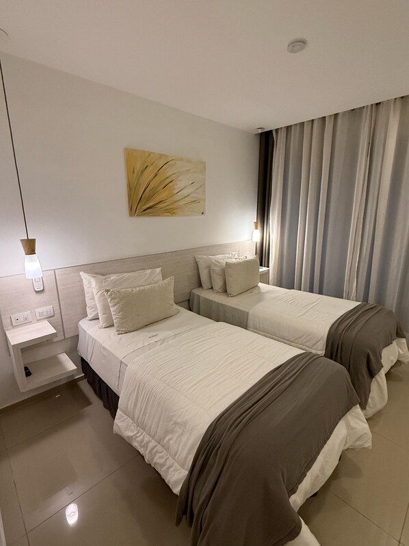 Een hotelkamer met twee bedden, een nachtkastje, een kunstwerk aan de muur en een raam met gordijnen.