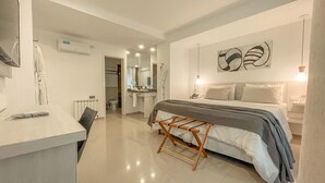 A modern bedroom with a bed, bedside tables, a desk, and a bathroom in the background. - La Olivia Hotel Boutique & Spa (La Falda)