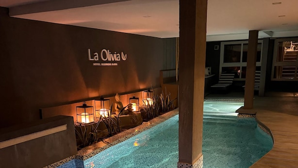 An indoor swimming pool with a tiled edge and a wooden deck area. - La Olivia Hotel Boutique & Spa (La Falda)