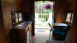 A compact kitchen with a sink, stove, and cabinets, leading to a balcony with a table and chairs. - La roulotte du petit bois (Thénouville)