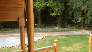 A wooden deck with a stone border and a grassy area with trees in the background. - La roulotte du petit bois (Thénouville)