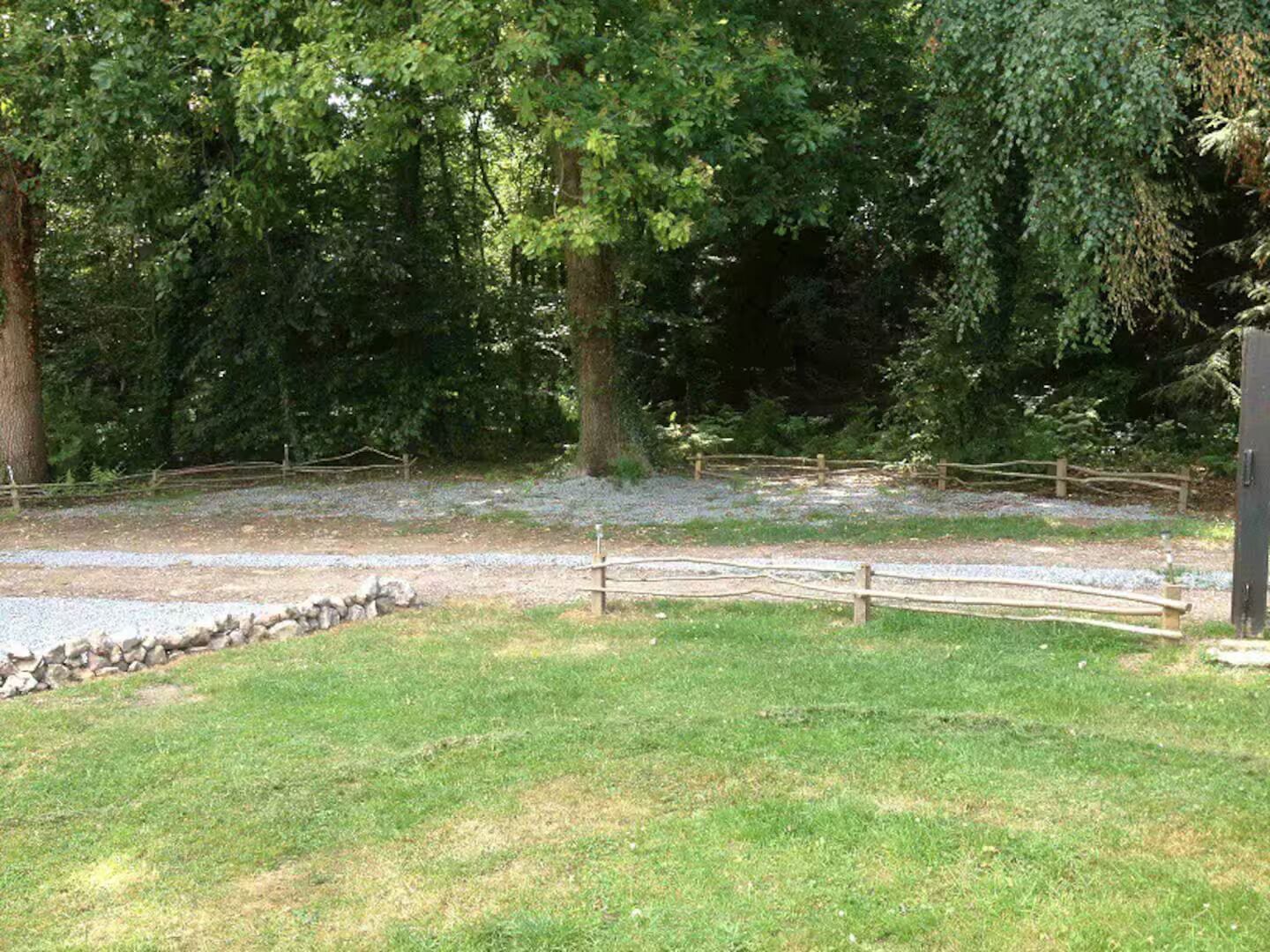 A fenced outdoor area with a gravel path, surrounded by trees and grass.