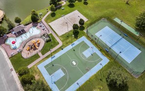 An aerial view of a park with multiple sports courts, a playground, and a lake.