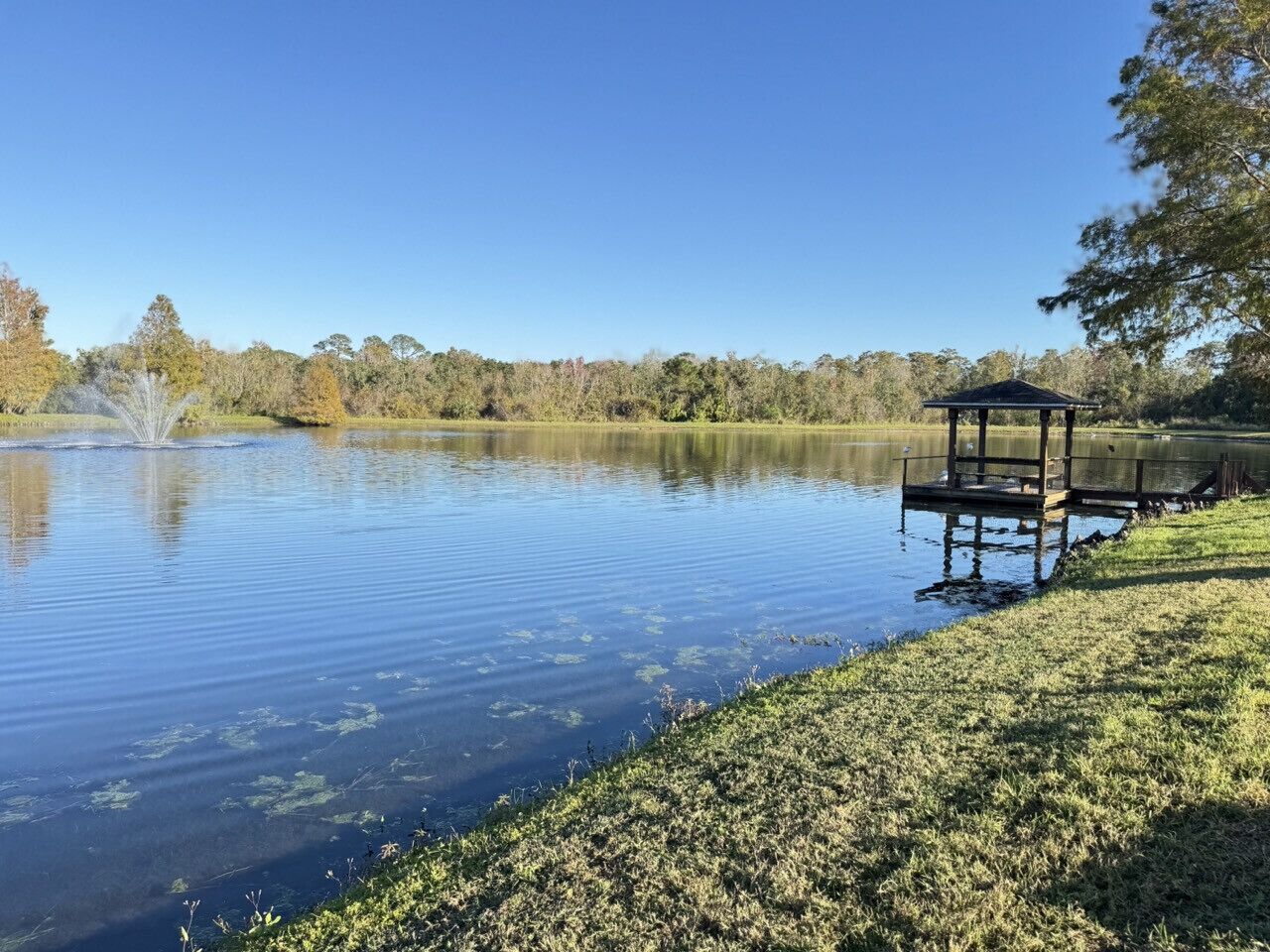 Un lago tranquilo con un pabellón a la derecha y una fuente en el centro.