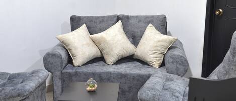 A grey sofa with three cushions, a small table with a glass vase, and a black door in the background.