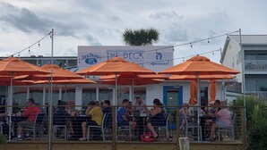 An outdoor dining area with orange umbrellas and tables, a sign for "The Deck" restaurant, and a view of a building in the background.