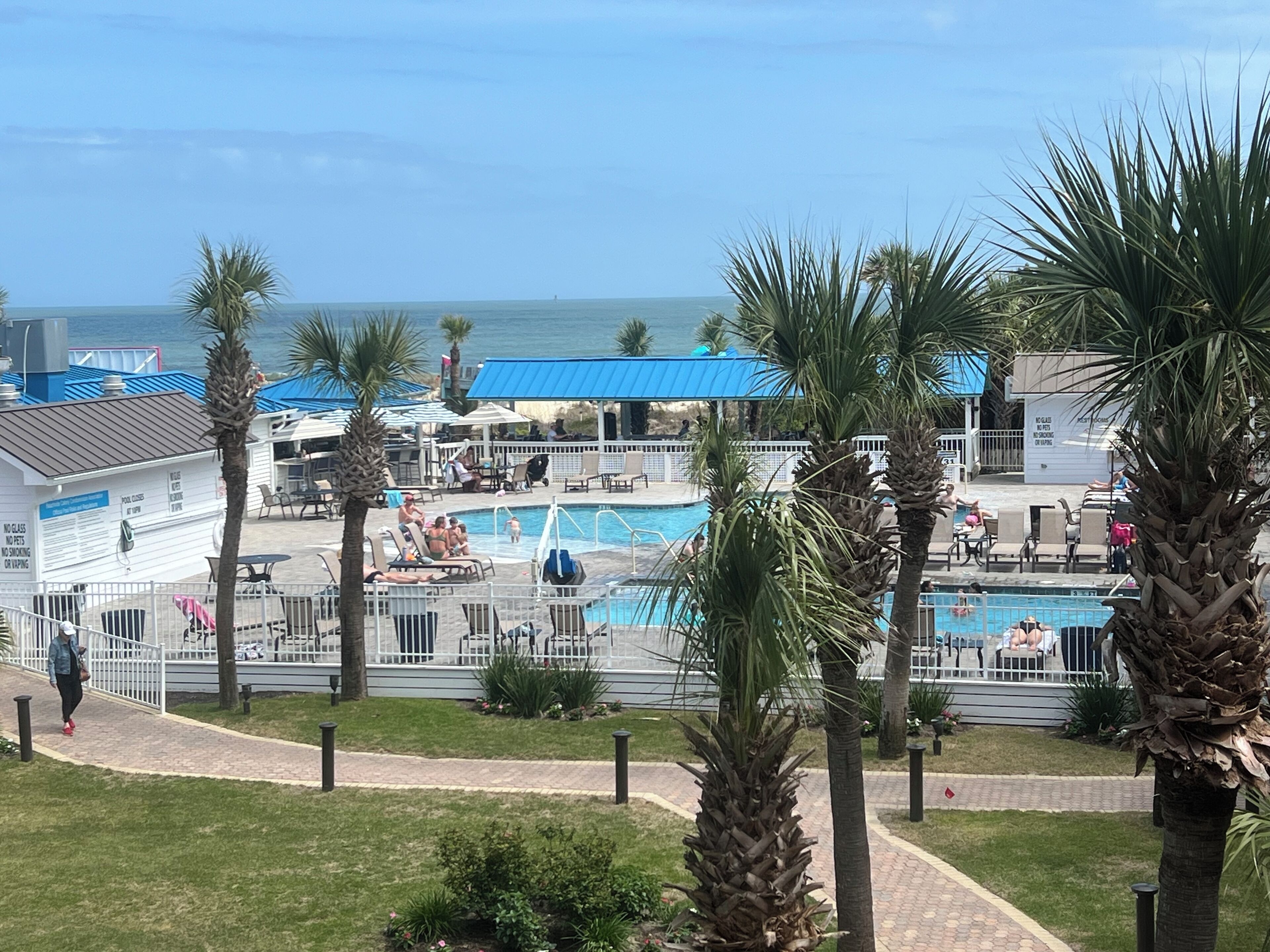 A pool area with multiple pools, palm trees, and a view of the ocean.