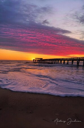 A beach scene with a pier extending into the water during sunset.