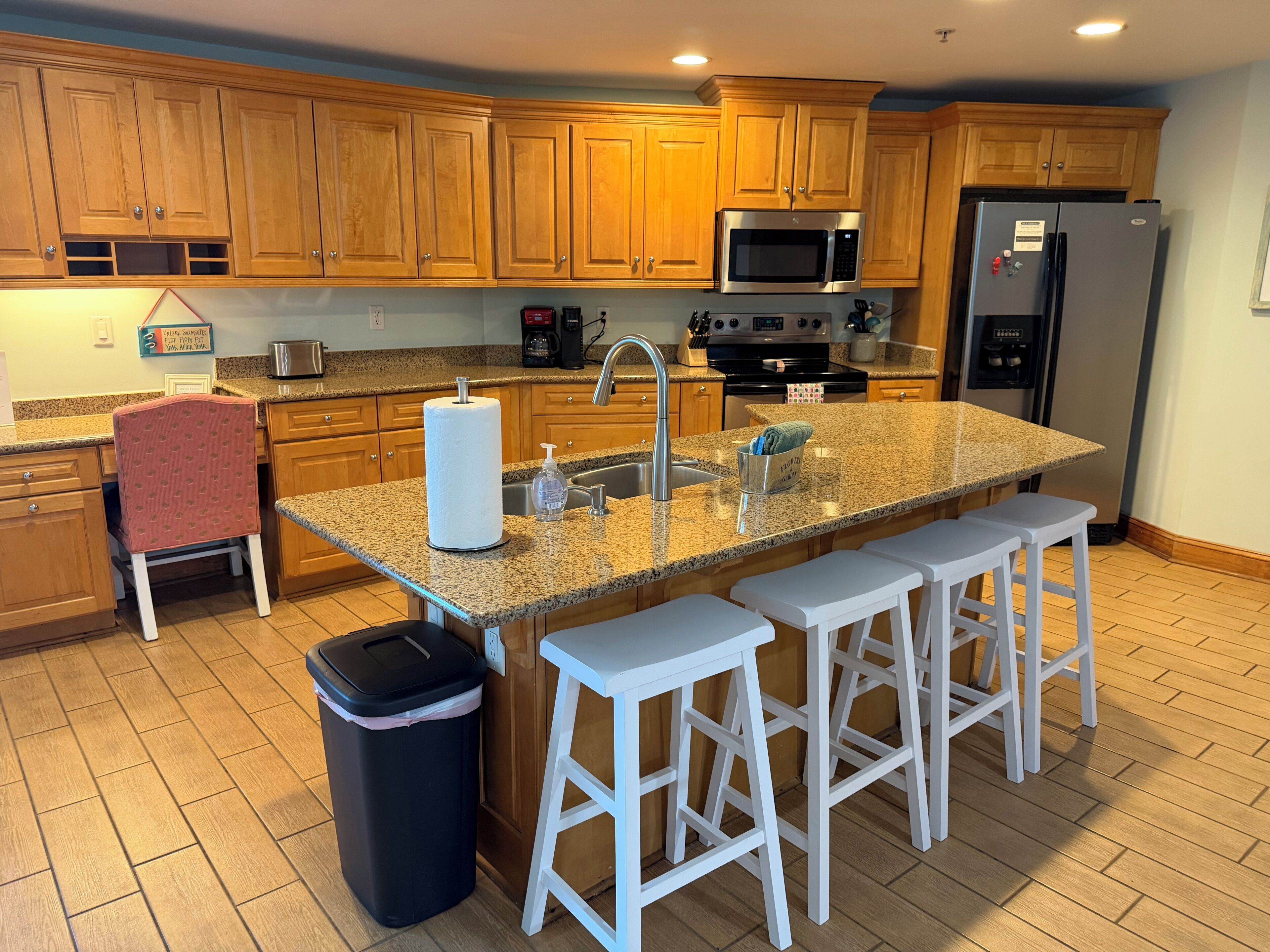 A kitchen with wooden cabinets, a stainless steel microwave, a refrigerator, and a granite countertop.