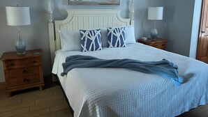 A neatly arranged bedroom with a large bed, two bedside tables, a nightstand, a painting above the bed, and a wooden door.