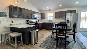 A modern kitchen with dark cabinets, a central island, stainless steel appliances, and pendant lighting.