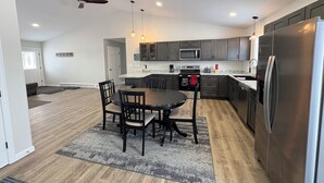 A modern kitchen with dark cabinets, a stainless steel refrigerator, and a dining area with a round table and chairs.