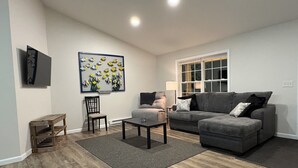 A living room with a grey sofa, a small table, a chair, and a wall-mounted picture of fish.