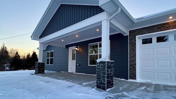 A two-story house with a dark exterior, a white garage door, and a stone pillar in front.