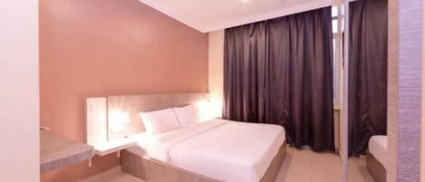Habitación de hotel con cama, mesita de noche, espejo y ventana con cortinas.