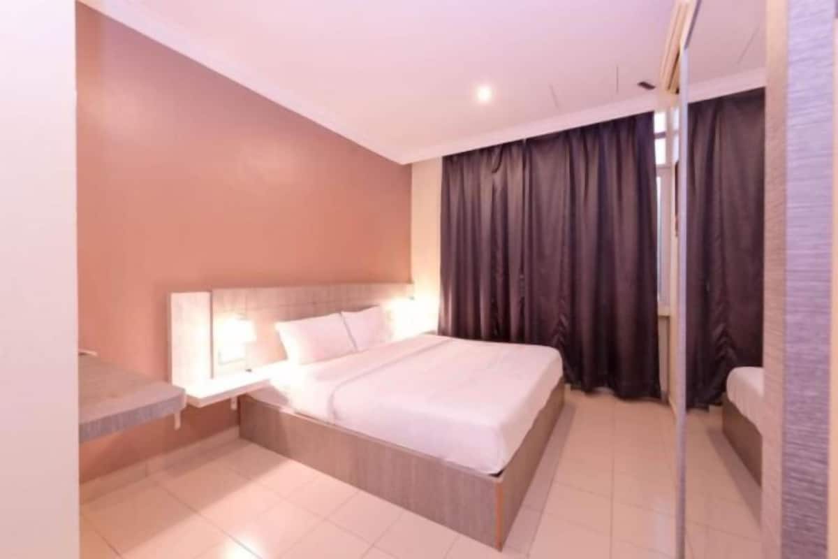 A hotel room with a bed, a bedside table, a mirror, and a window with curtains.