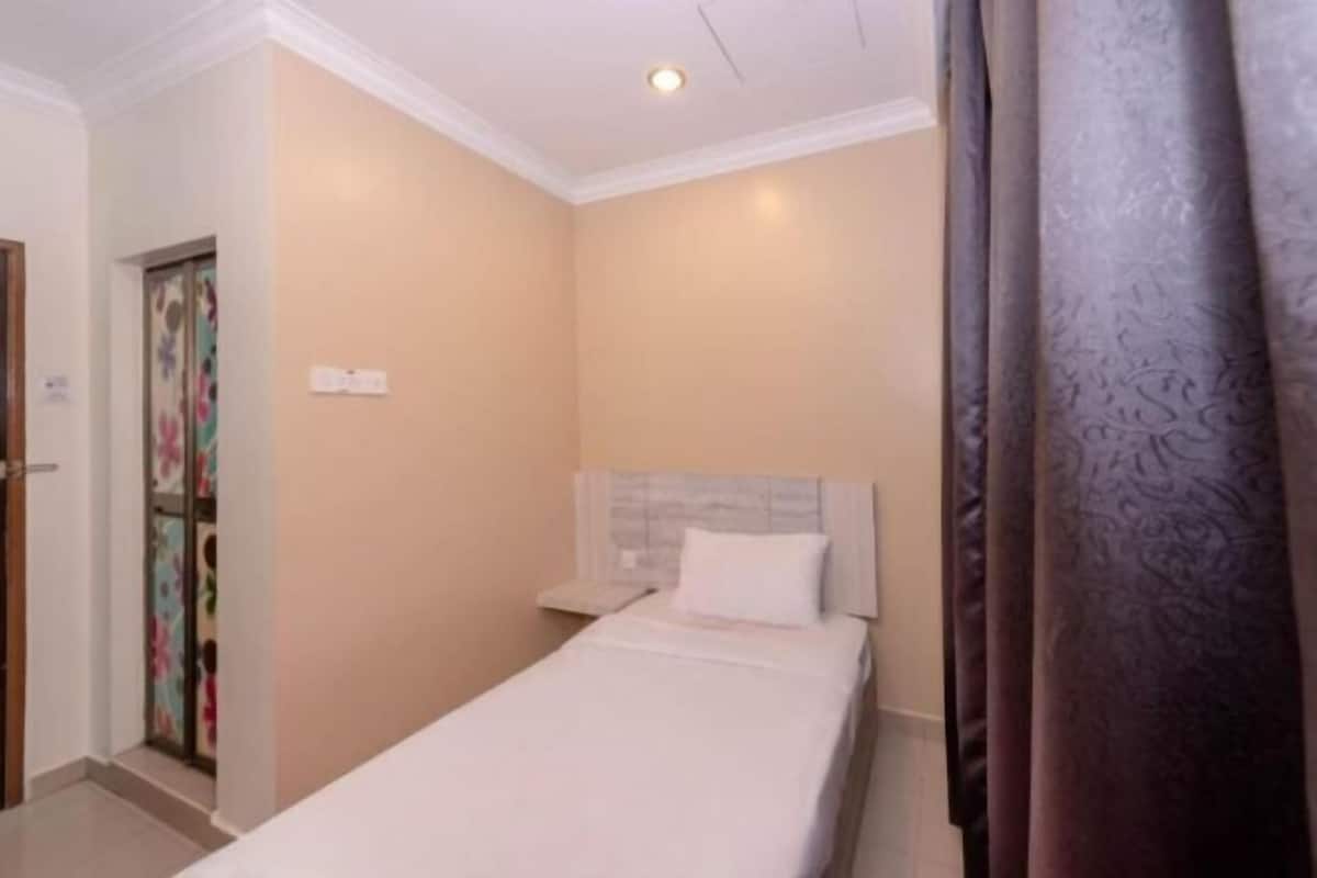 A single bed with a headboard, a nightstand, a door with a floral pattern, and a curtain.