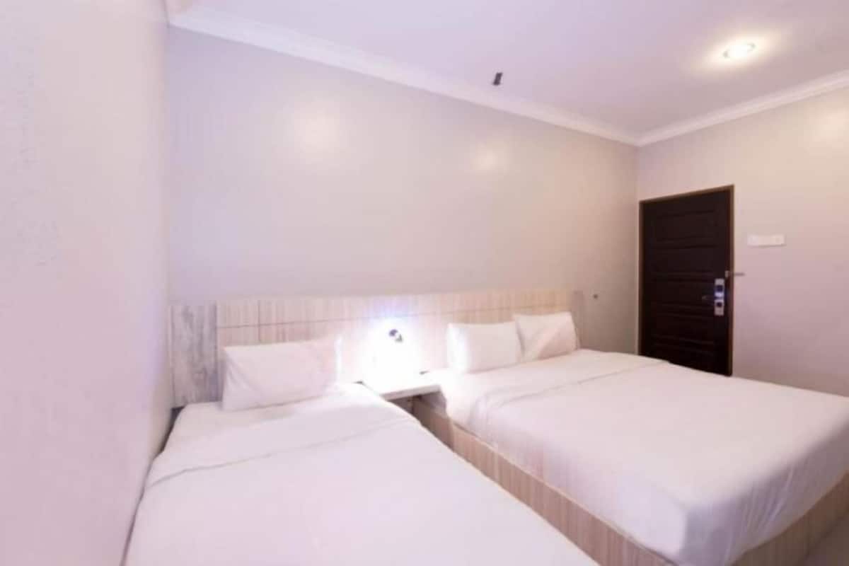 A hotel room with two beds, a nightstand, a door, and a light fixture.