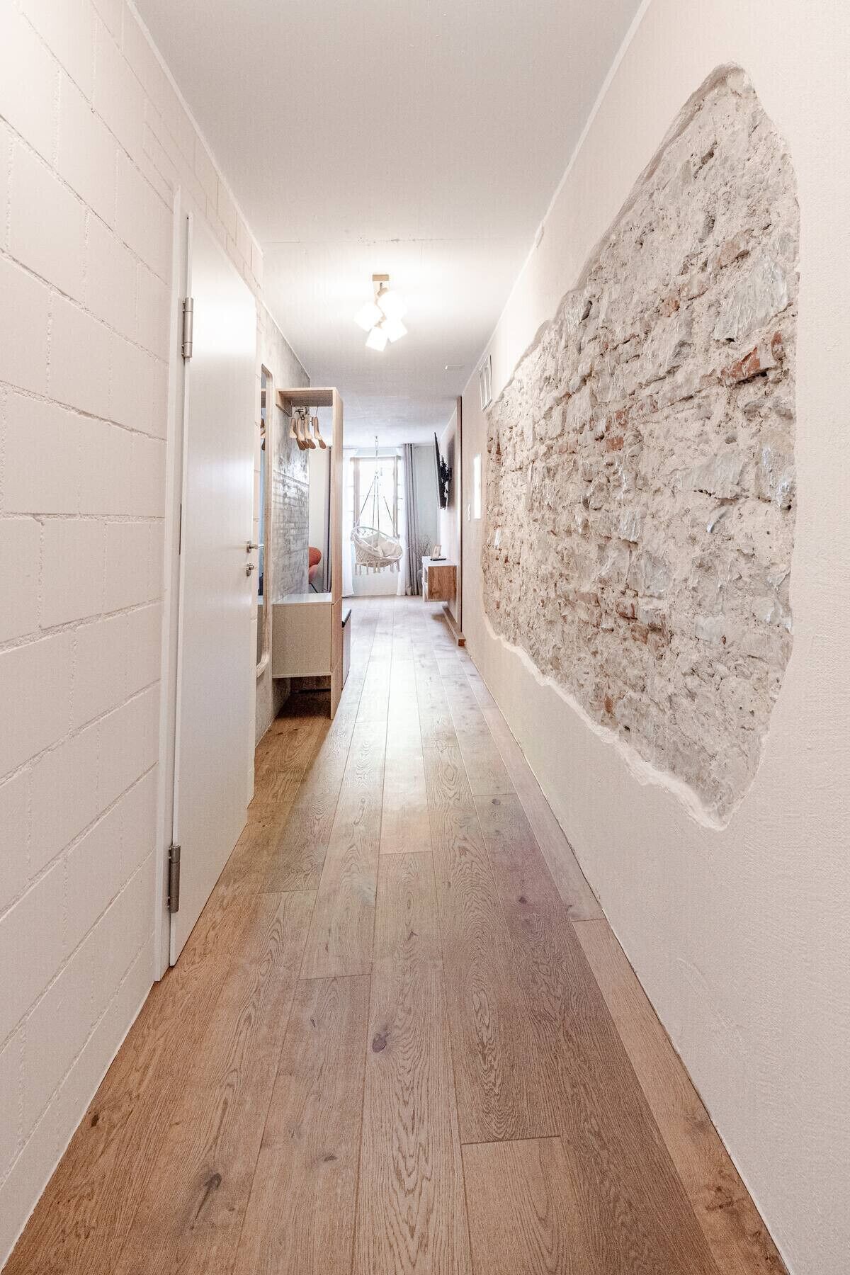 A hallway with wooden flooring, a white brick wall, and a textured stone wall.