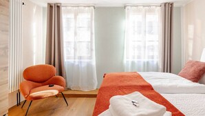 A hotel room with a bed, a chair, and a window with curtains. - Marllon Suites – Casa Rheinblick Apartments – Bella Suite (Basel)