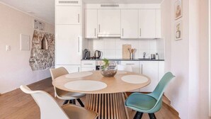 A modern kitchen with white cabinets, a round wooden dining table, and two chairs. - Marllon Suites – Casa Rheinblick Apartments – Bella Suite (Basel)