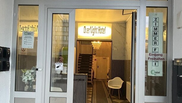 L’entrée d’un hôtel, avec une enseigne indiquant « Hôtel – Nuitée » et le numéro « 79 » au-dessus de la porte.