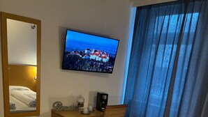 Une chambre d’hôtel avec un lit, un bureau équipé d’un ordinateur, une chaise, une télévision et une fenêtre avec des rideaux.