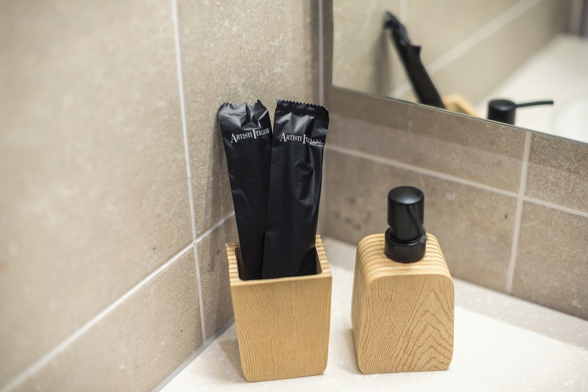 A bathroom with a wooden soap dispenser and two black toiletry bags in a holder.
