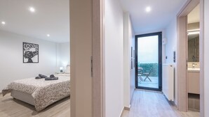 A modern hotel room with a bed, a nightstand, a lamp, and a view of the outdoors. - PetraLab By Greece Apartment (Athens)