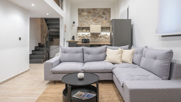 A modern living room with a grey sectional sofa, a round black coffee table, and a staircase leading to an upper floor. - PetraLab By Greece Apartment (Athens)