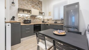 A modern kitchen with grey cabinets, a stone accent wall, and a stainless steel refrigerator. - PetraLab By Greece Apartment (Athens)