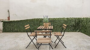 A small outdoor seating area with a wooden table and four chairs, surrounded by a green hedge and a white wall. - PetraLab By Greece Apartment (Athens)
