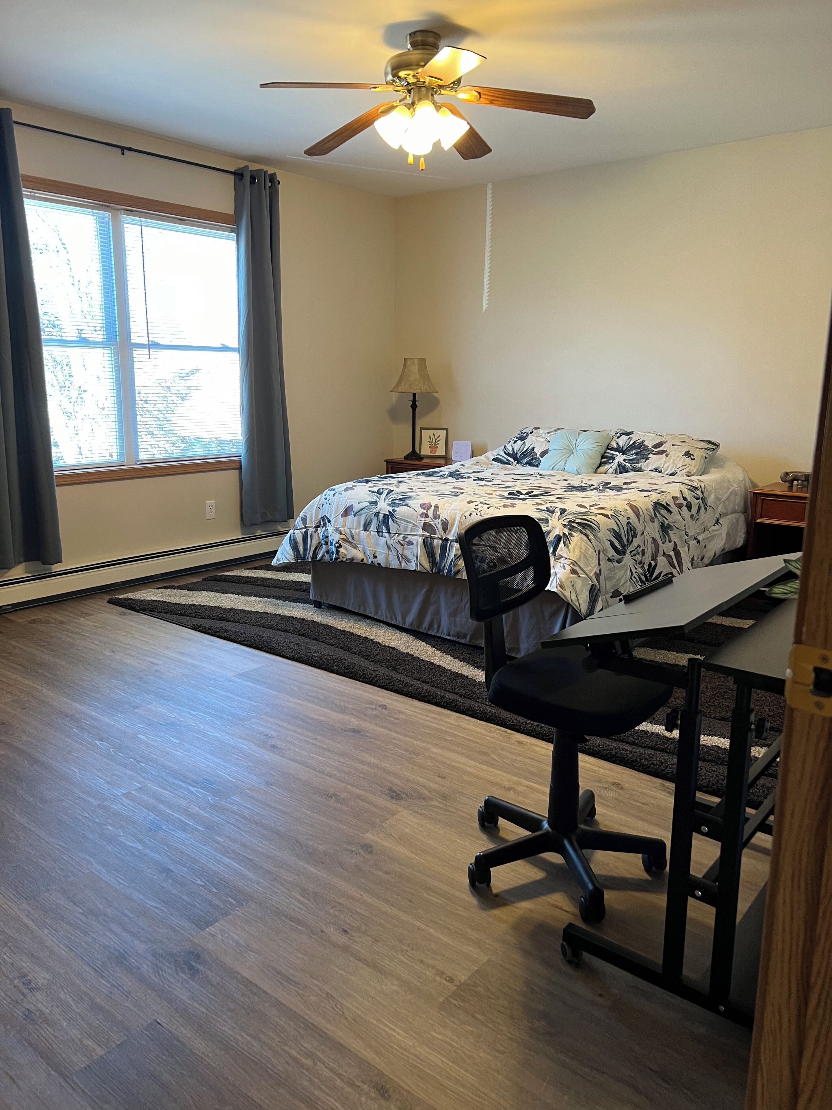 A bedroom with a bed, desk, chair, and ceiling fan.